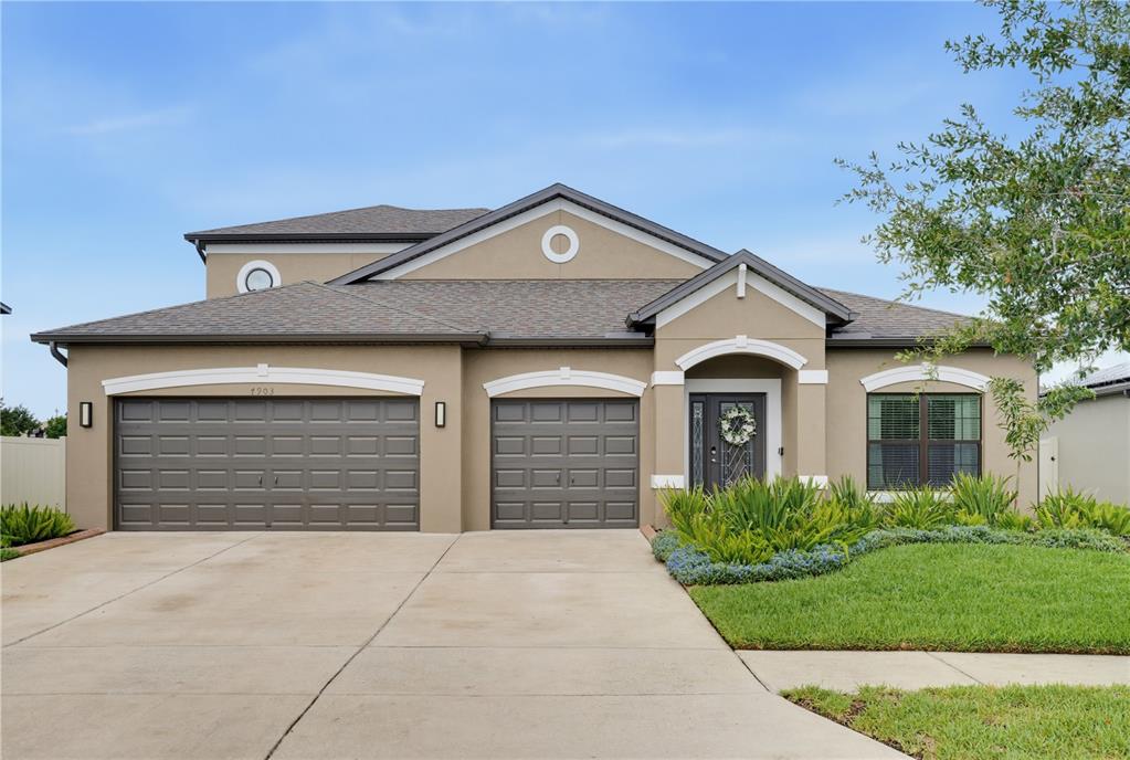 A tan stucco house with a three-car garage and a front entrance under a portico — 7903 LAGO MIST WAY, WESLEY CHAPEL, FL