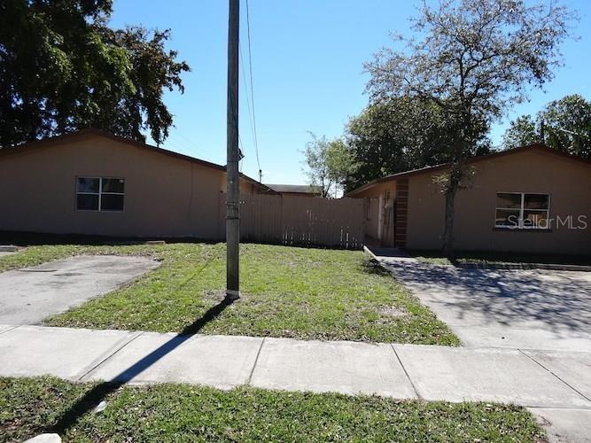 Two single-story tan buildings are separated by a wooden fence and a grassy yard — 2400 NW 21ST STREET UNIT 3, FORT LAUDERDALE, FL