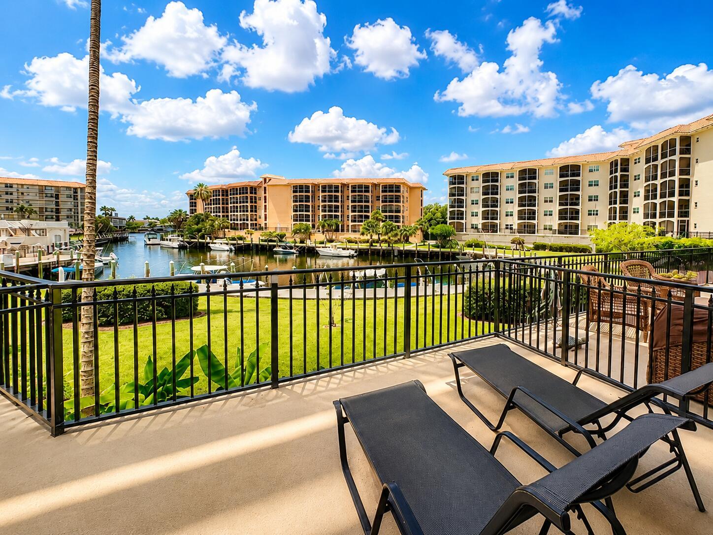 A balcony with two lounge chairs overlooks a grassy lawn, a canal, and apartment buildings — 2871 N Ocean Boulevard # M132, Boca Raton FL 33431, BOCA RATON, FL