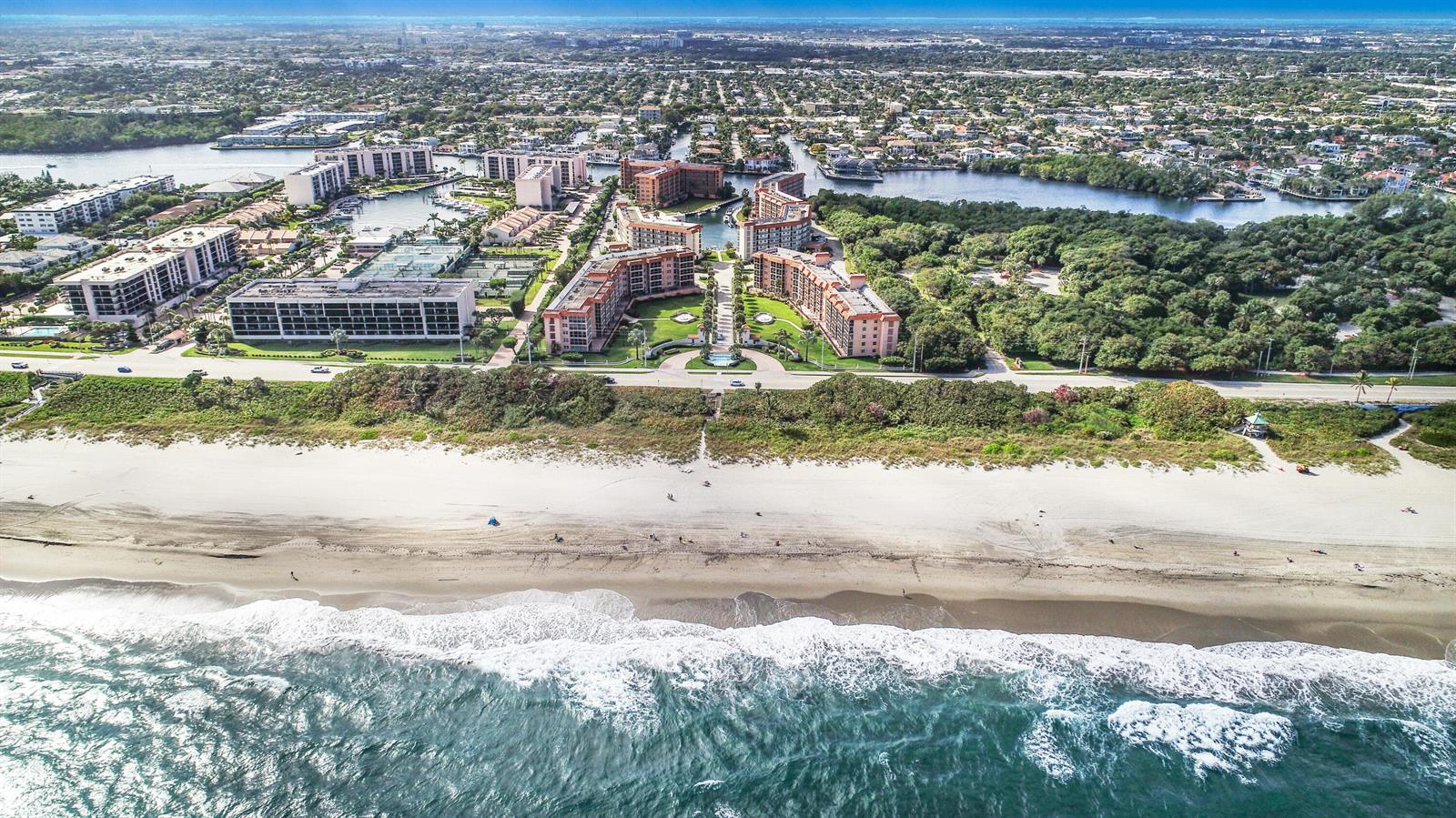 An aerial view of beachfront condominium buildings surrounded by lush trees and a coastal waterway — 2871 N Ocean Boulevard # M132, Boca Raton FL 33431, BOCA RATON, FL
