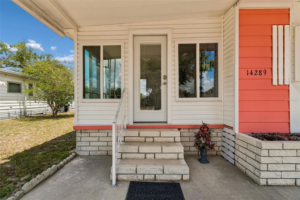 The exterior of a home features white siding, a front door, and concrete steps — 14289 MIDFIELD STREET, BROOKSVILLE, FL