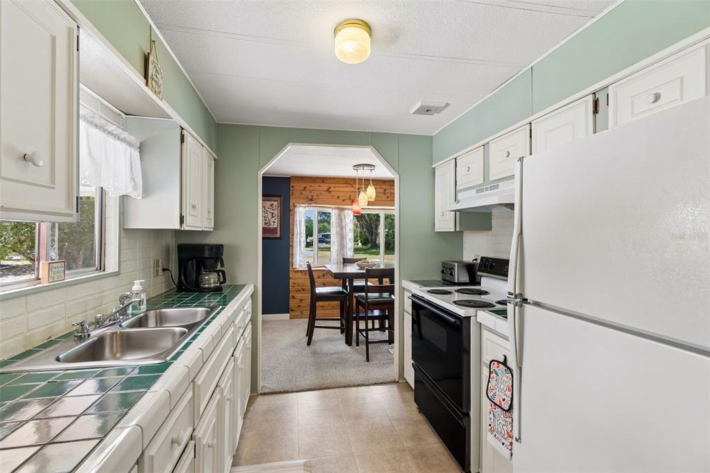 A kitchen with white cabinets, green tile countertops, and a view into a dining area — 14289 MIDFIELD STREET, BROOKSVILLE, FL