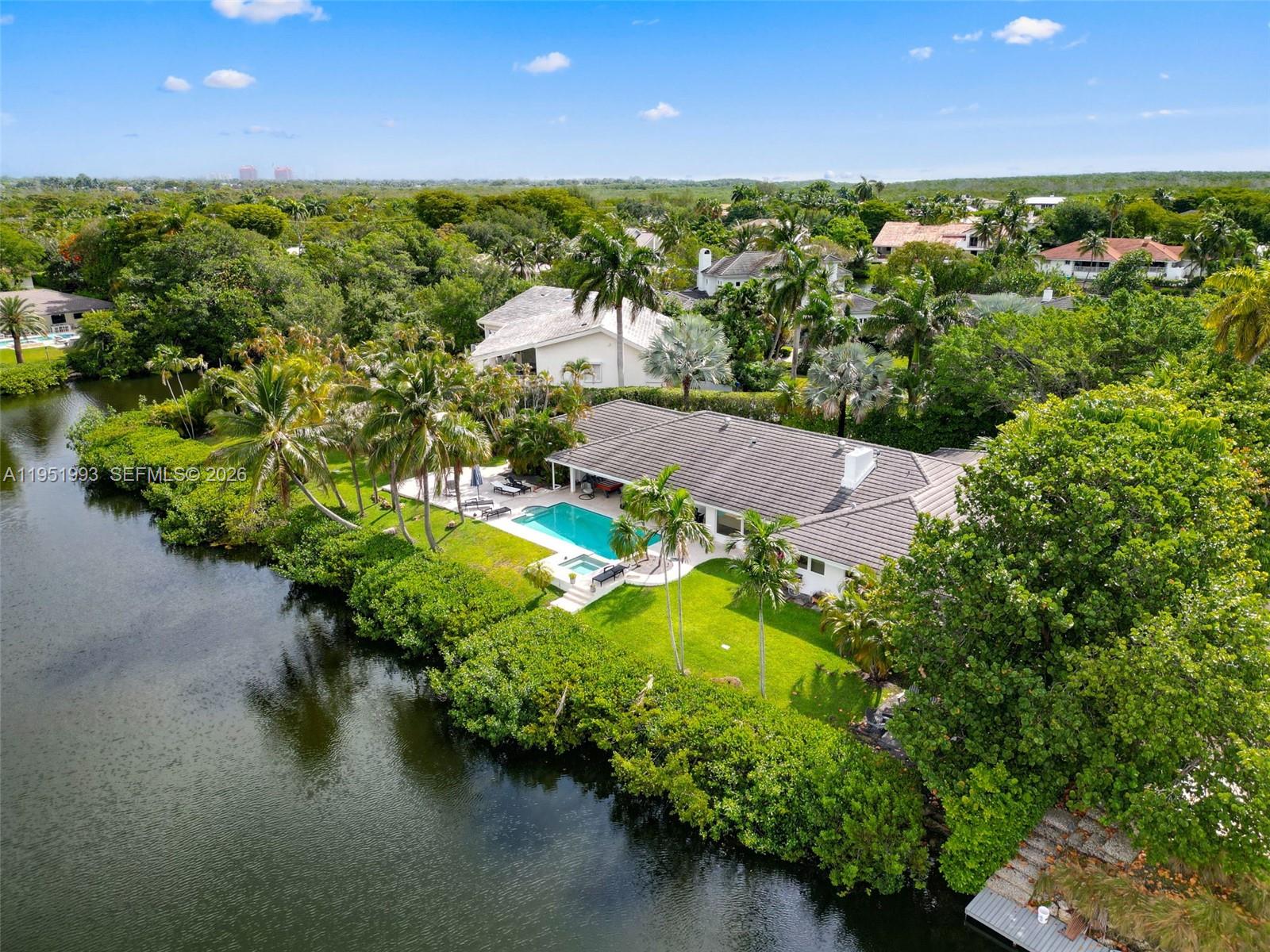 An aerial view shows a house with a pool and lawn situated beside a canal — 415 Rovino Ave, Coral Gables FL 33156, CORAL GABLES, FL