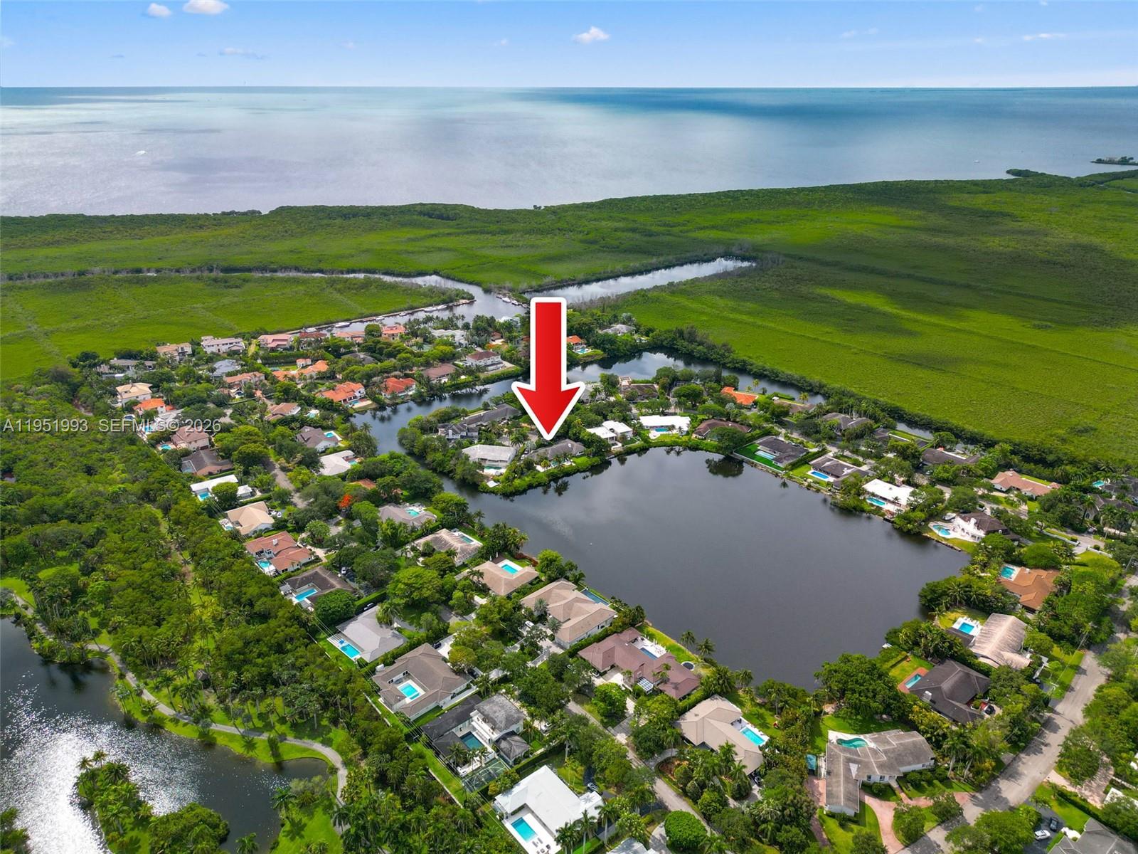 An aerial view shows a residential neighborhood with houses surrounding a lake near the coast — 415 Rovino Ave, Coral Gables FL 33156, CORAL GABLES, FL