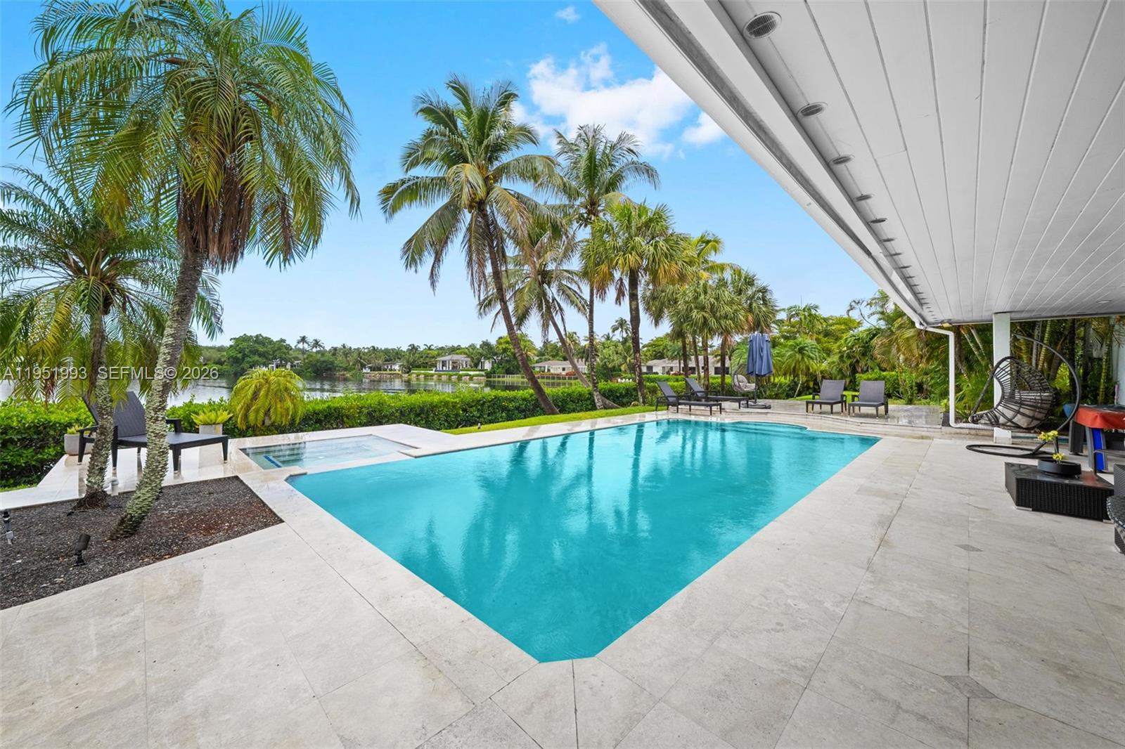 A swimming pool and spa sit on a stone patio overlooking a lake and palms — 415 Rovino Ave, Coral Gables FL 33156, CORAL GABLES, FL