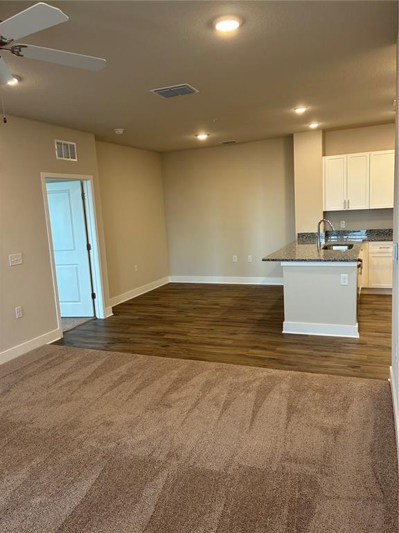 An open-concept living area features carpeted flooring, a wood-floored kitchen, and white cabinetry — 2280 WATERFALL COURT UNIT 4-302, MOUNT DORA, FL