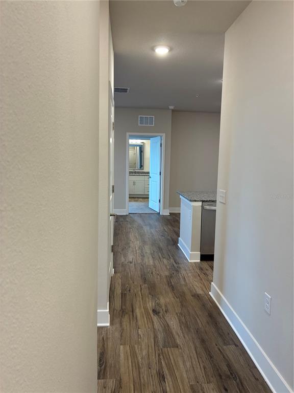 A hallway with wood-look flooring leads to a kitchen and a bathroom beyond — 2280 WATERFALL COURT UNIT 4-302, MOUNT DORA, FL