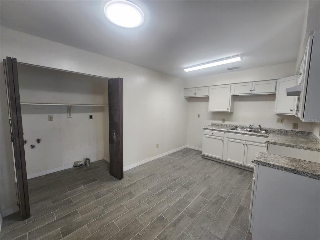A kitchen features white cabinets, granite-look countertops, gray tile flooring, and a laundry closet — 5817 NW 23 TERRACE UNIT 2, GAINESVILLE, FL