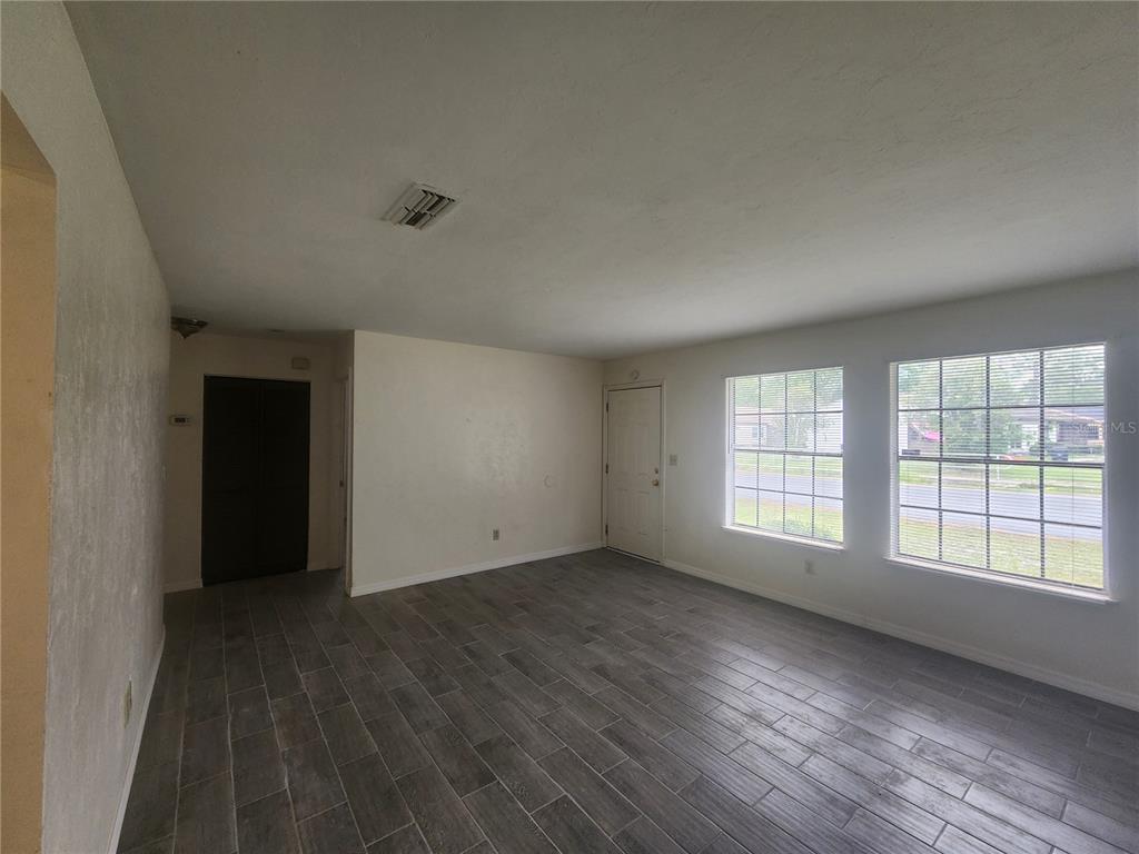 An empty living room features gray wood-look tile flooring, white walls, and two large windows — 5817 NW 23 TERRACE UNIT 2, GAINESVILLE, FL