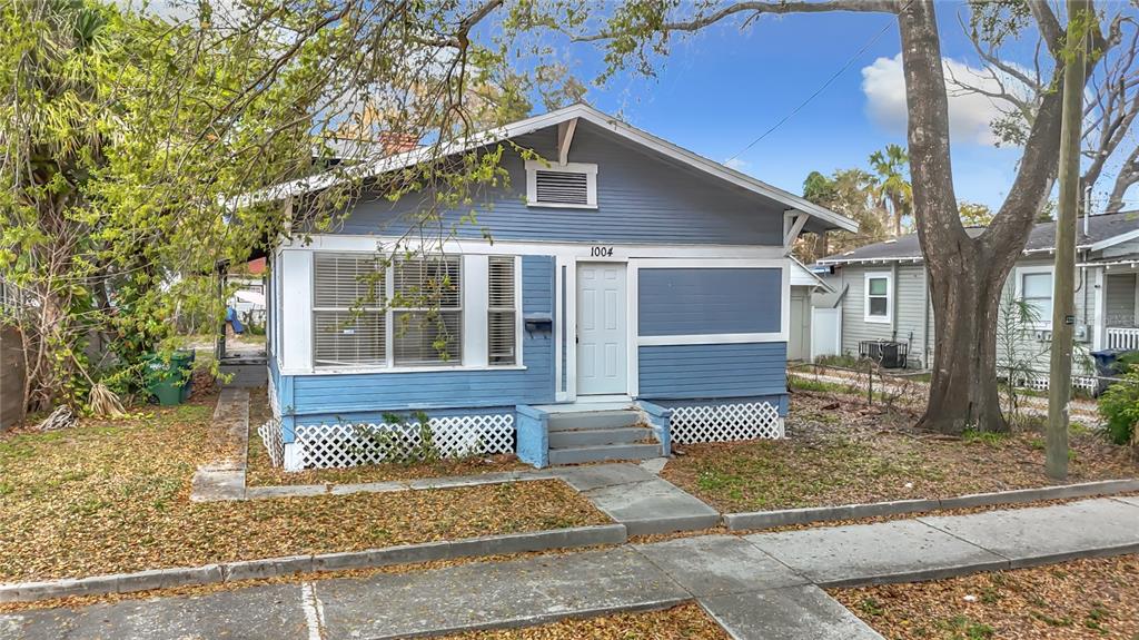 A blue, single-story bungalow with a front porch, lattice skirting, and a concrete walkway — 1004 E 22ND AVENUE, TAMPA, FL