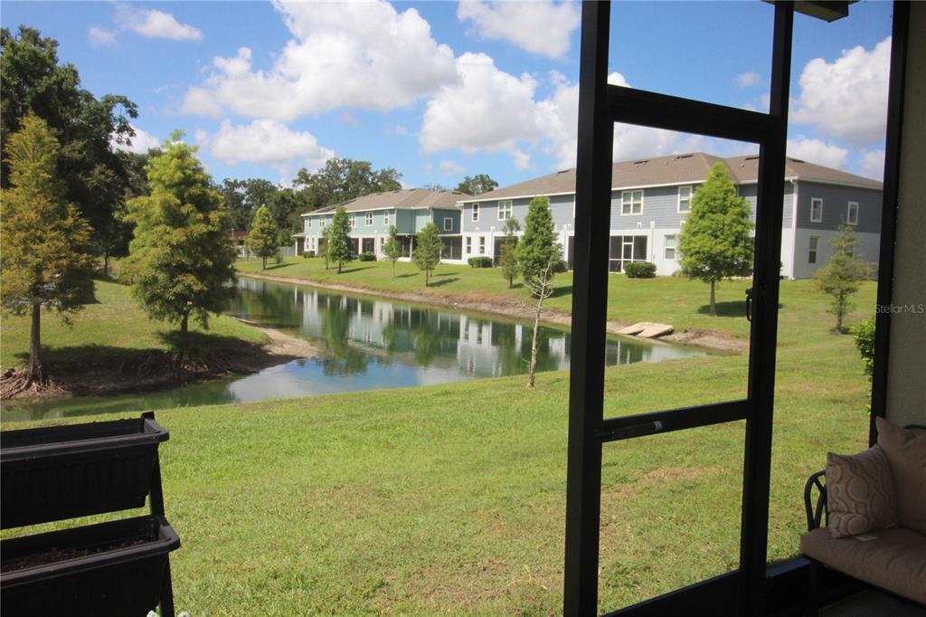 A view from a screened-in porch overlooking a grassy lawn, a pond, and apartment buildings — 2135 LACEFLOWER DRIVE, BRANDON, FL
