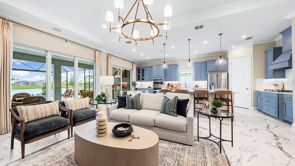 An open-concept living room and kitchen feature blue cabinetry, a large chandelier, and sliding doors — 26124 ASPARANO AVENUE, ENGLEWOOD, FL
