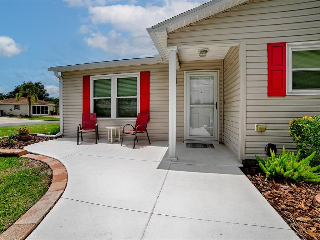 A beige house exterior features a concrete patio, red shutters, and a front entrance — 1070 BERKSHIRE PLACE, THE VILLAGES, FL