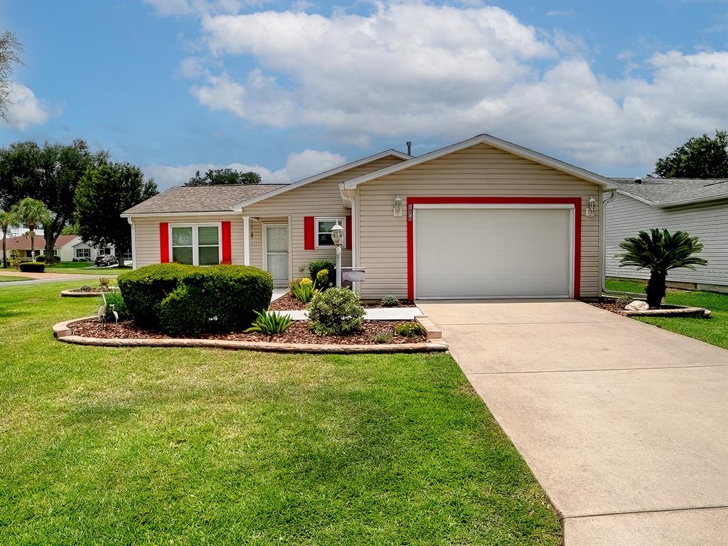A single-story house with beige siding, red shutters, a garage, and a landscaped front yard — 1070 BERKSHIRE PLACE, THE VILLAGES, FL