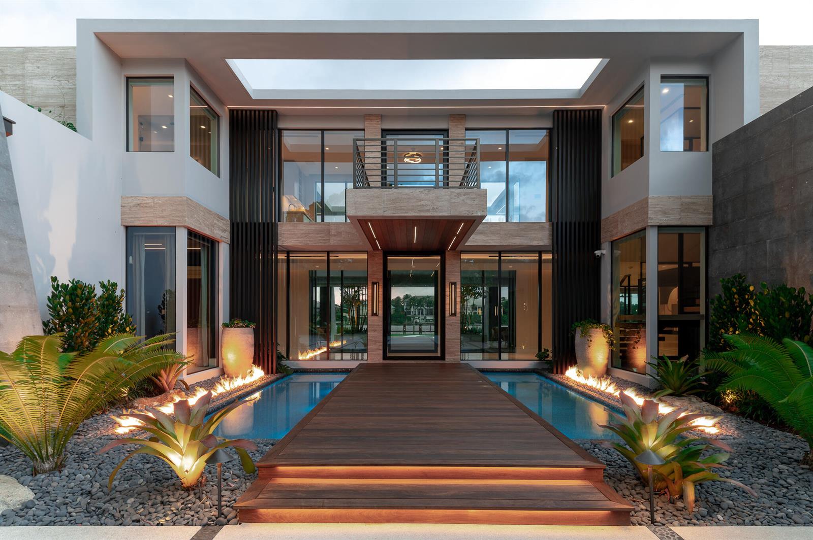 A modern house exterior features a wooden walkway over a pool with integrated fire pits — 488 S Beach Road, Jupiter Island FL 33455, JUPITER ISLAND, FL