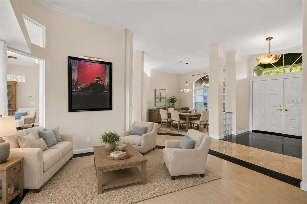 A living room and dining area feature light-colored furniture, hardwood floors, and a double-door entrance — 5501 STAG THICKET LANE, PALM HARBOR, FL