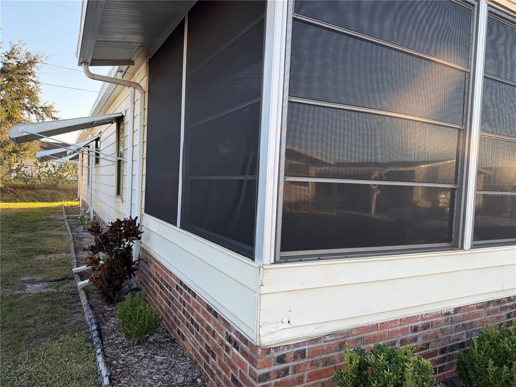 The exterior of a home features a screened-in porch, brick skirting, and light-colored siding — 4165 ROLLING OAKS DRIVE, WINTER HAVEN, FL