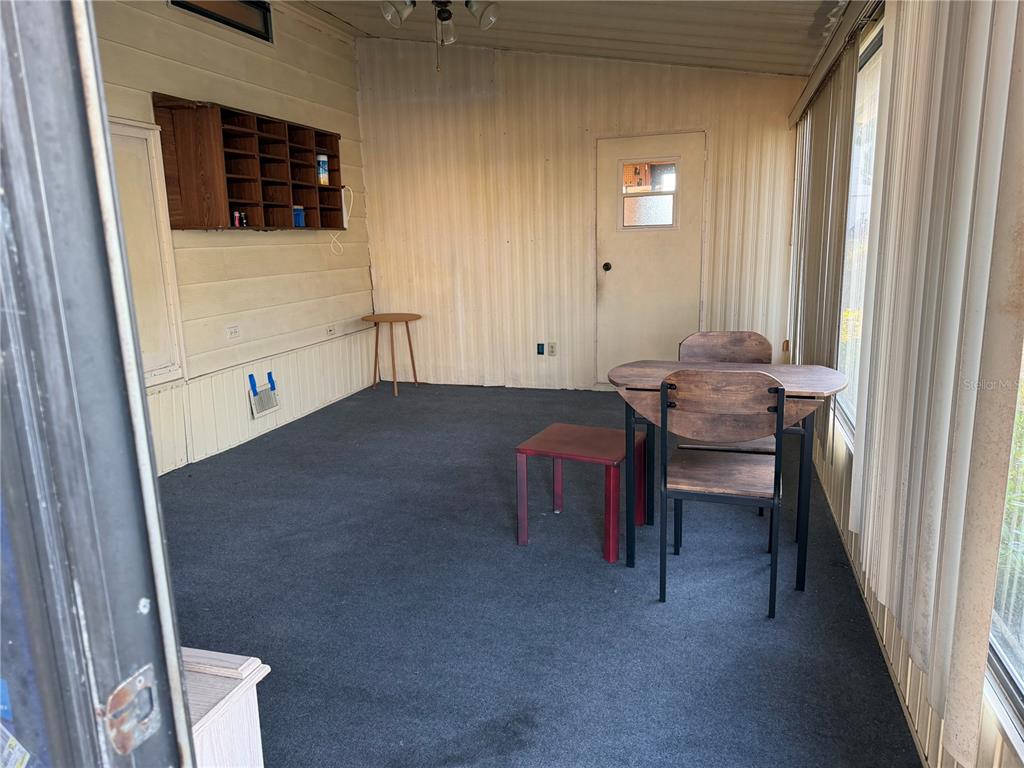 A sunroom with paneled walls, gray carpeting, a small dining set, and wall-mounted shelving — 4165 ROLLING OAKS DRIVE, WINTER HAVEN, FL