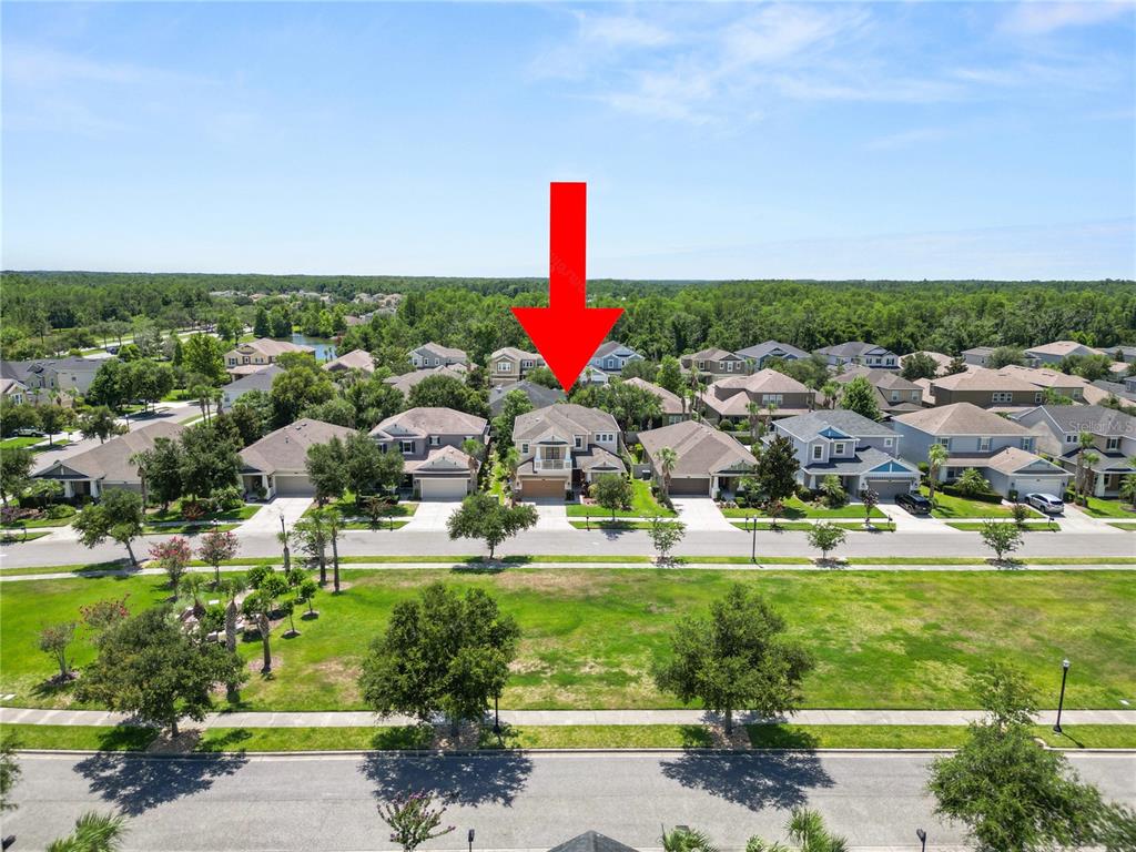 An aerial view shows a two-story suburban house with a balcony facing a grassy park — 8775 SENTIERO DRIVE, LAND O LAKES, FL