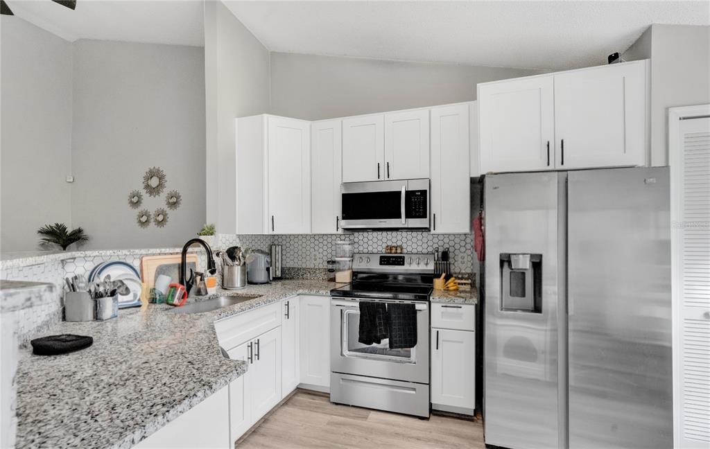 A kitchen with white cabinets, granite countertops, stainless steel appliances, and a hexagonal tile backsplash — 9616 RIVER WALK COURT, ORLANDO, FL