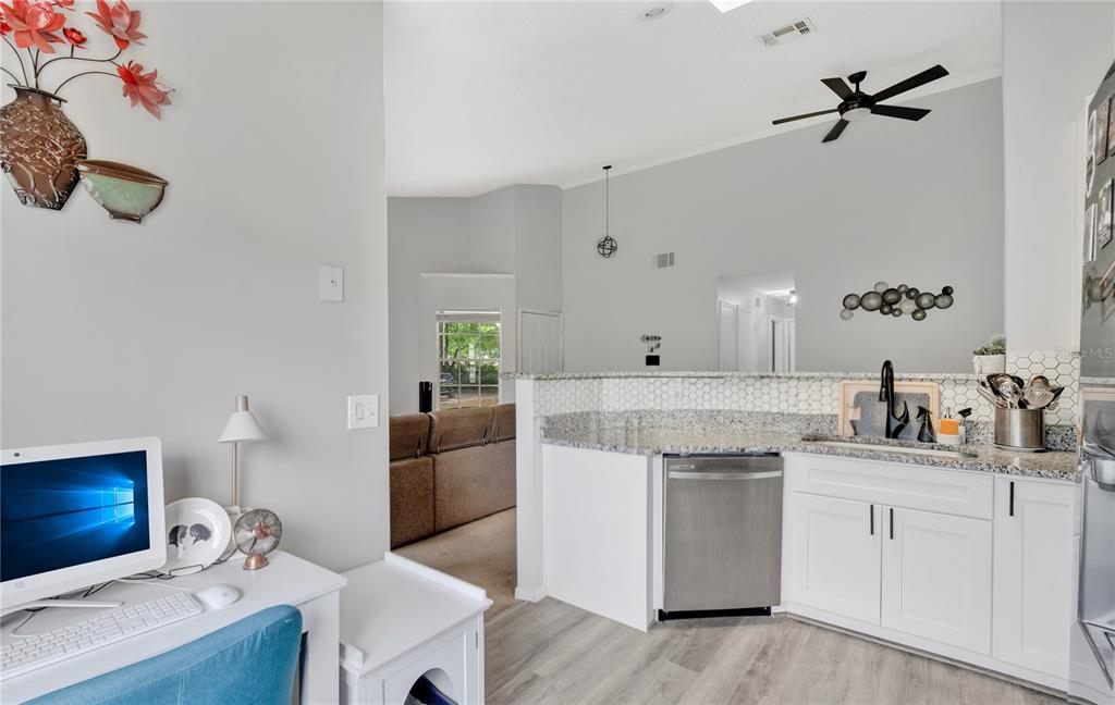 A kitchen with white cabinets and granite countertops sits adjacent to a small home office — 9616 RIVER WALK COURT, ORLANDO, FL