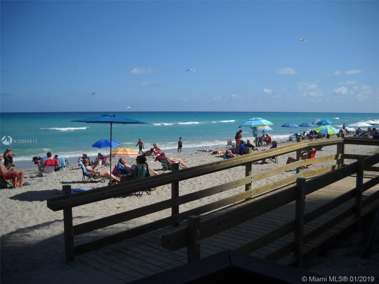 A wooden boardwalk leads to a sandy beach filled with people, umbrellas, and the ocean — 3901 S Ocean Dr # 12D, Hollywood FL 33019, HOLLYWOOD, FL