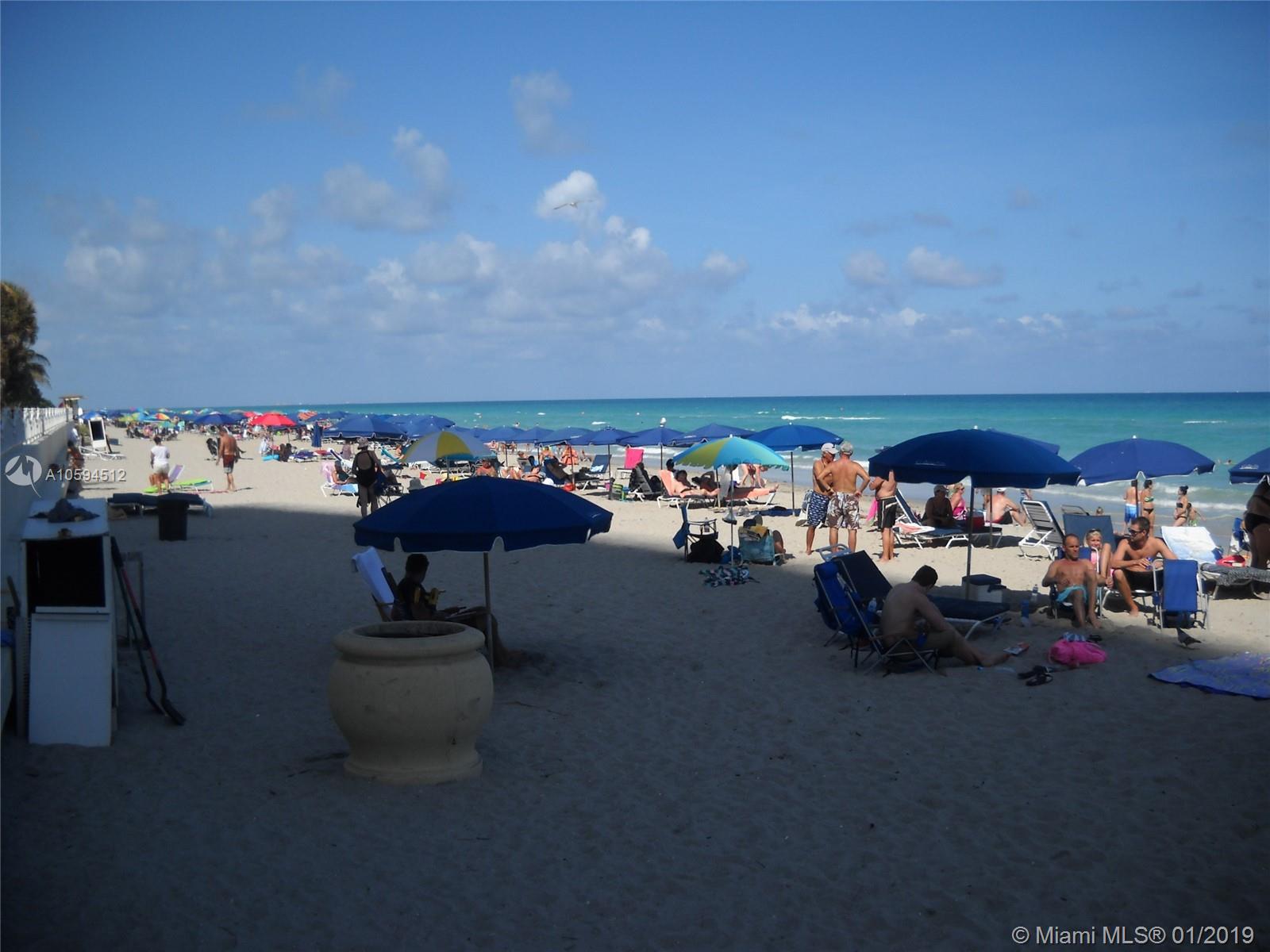A sunny beach scene with many people relaxing under colorful umbrellas on the sand — 3901 S Ocean Dr # 12D, Hollywood FL 33019, HOLLYWOOD, FL