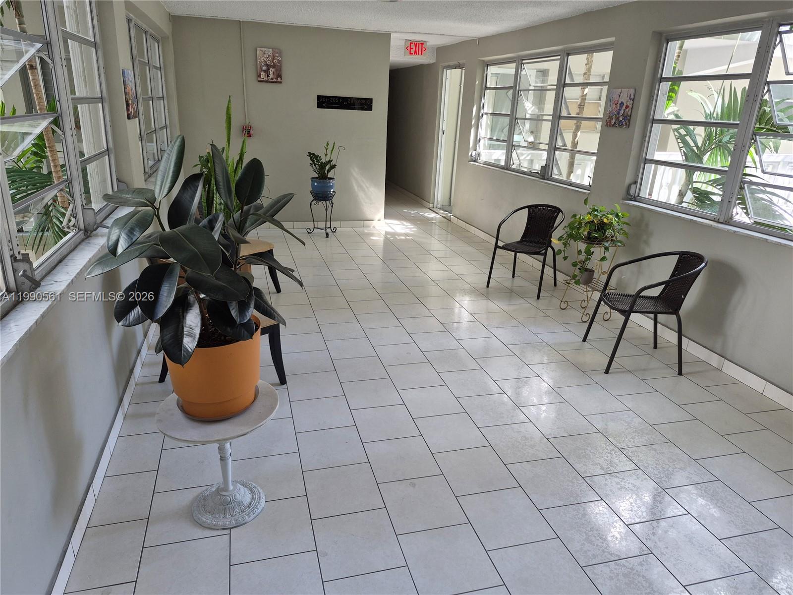A bright, tiled hallway features large windows, potted plants, and several chairs — 330 SE 2nd St # 202E, Hallandale Beach FL 33009, HALLANDALE BEACH, FL