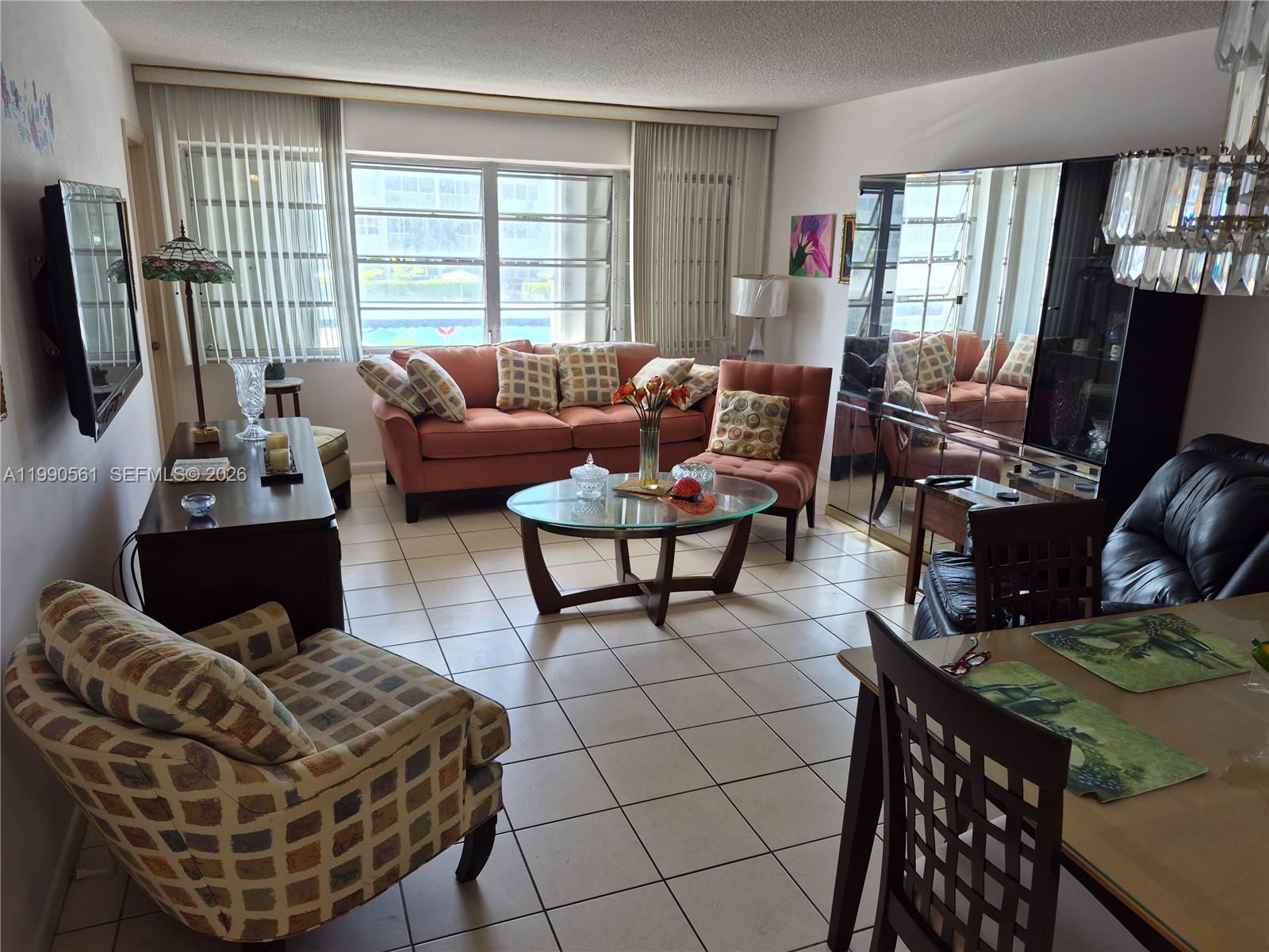 A living and dining area features tile floors, a coral sofa, and large window blinds — 330 SE 2nd St # 202E, Hallandale Beach FL 33009, HALLANDALE BEACH, FL