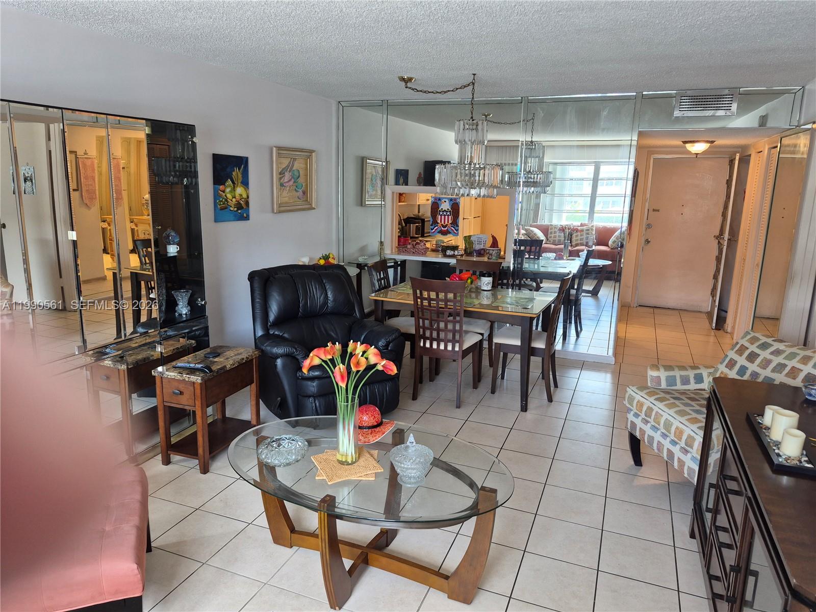 A living and dining area features tiled floors, a glass coffee table, and mirrored walls — 330 SE 2nd St # 202E, Hallandale Beach FL 33009, HALLANDALE BEACH, FL