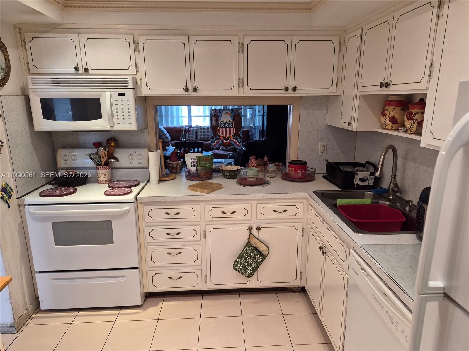 A kitchen features white cabinetry, a white stove, a double sink, and a pass-through window — 330 SE 2nd St # 202E, Hallandale Beach FL 33009, HALLANDALE BEACH, FL