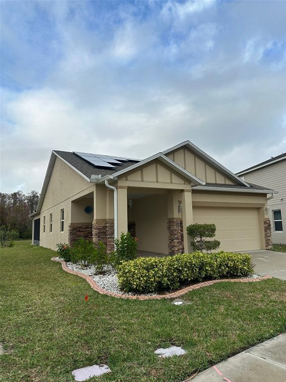 A tan single-story house with stone accents, a two-car garage, and roof-mounted solar panels — 2221 CANYON BREEZE AVENUE, KISSIMMEE, FL