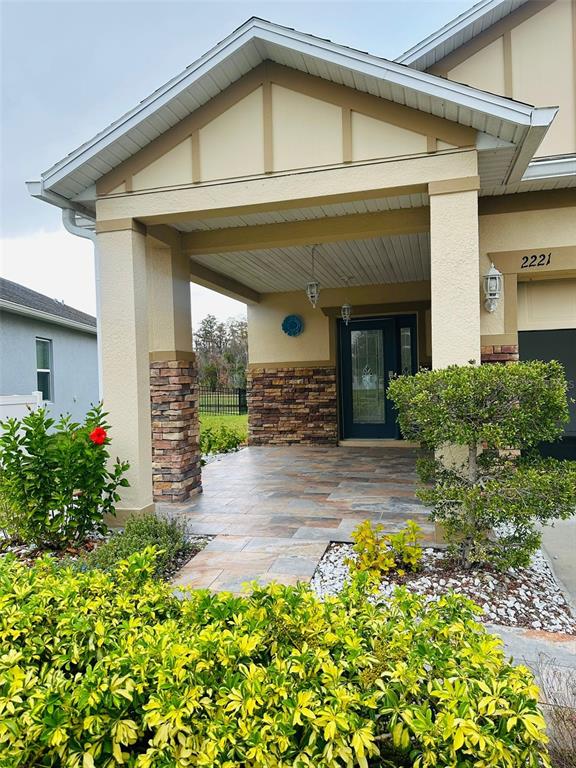 The exterior of a house features a covered porch with stone pillars and tiled flooring — 2221 CANYON BREEZE AVENUE, KISSIMMEE, FL