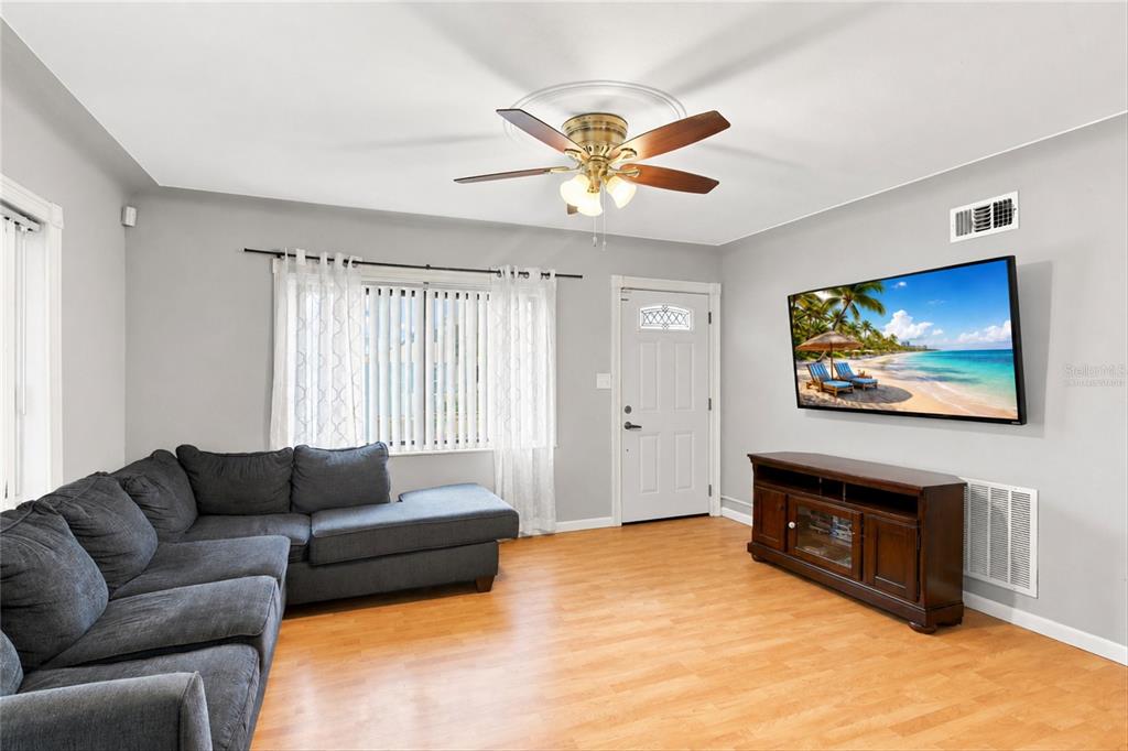 A living room with light wood flooring, a dark sectional sofa, and a ceiling fan — 3827 38TH AVENUE N, ST PETERSBURG, FL