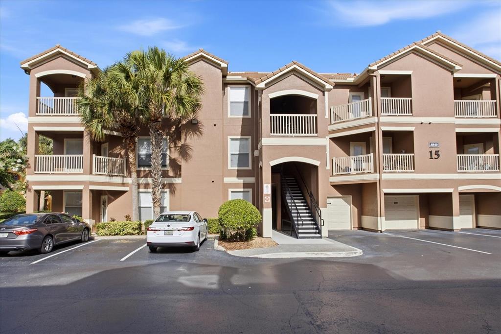 A three-story apartment building with tan stucco walls, balconies, and a parking lot — 8849 VILLA VIEW CIRCLE UNIT 203, ORLANDO, FL