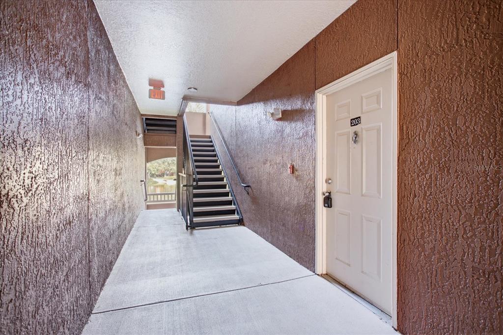 An outdoor apartment hallway features a white door labeled 203 and a metal staircase — 8849 VILLA VIEW CIRCLE UNIT 203, ORLANDO, FL