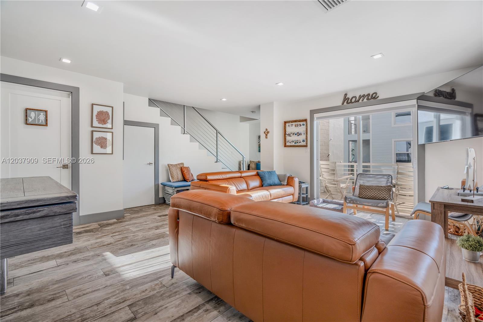 A living room features leather sofas, wood-look flooring, a staircase, and a sliding glass door — 94825 Overseas #254, Key Largo FL 33037, KEY LARGO, FL