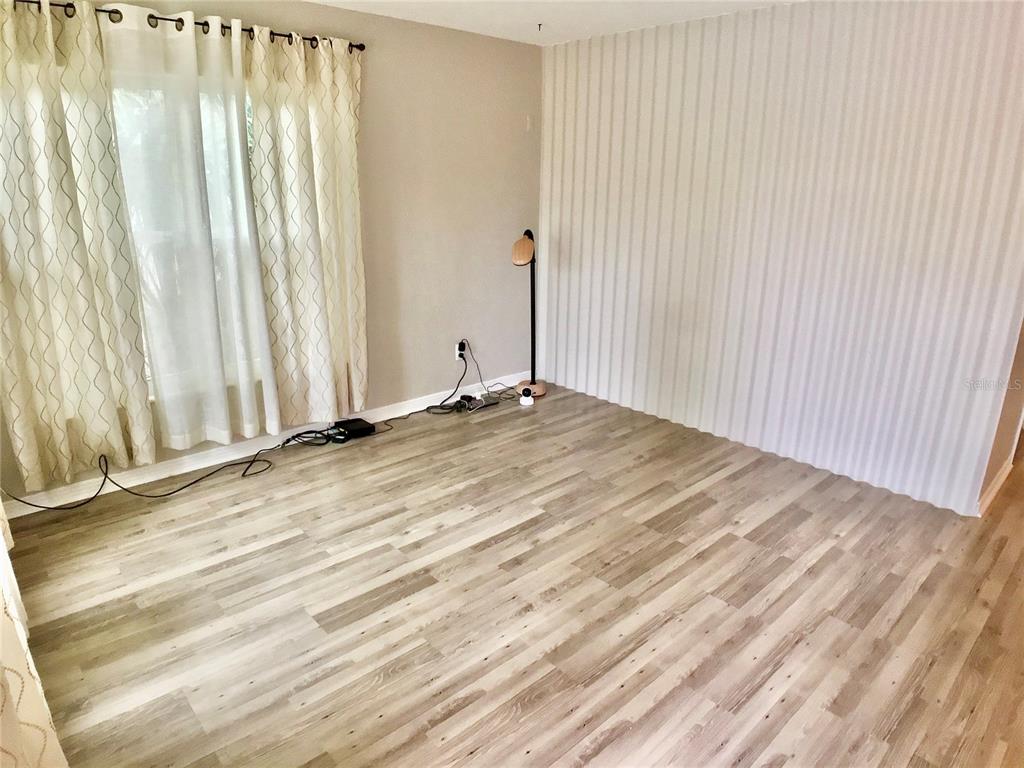 An empty room features light wood-look flooring, a striped accent wall, and floor-length curtains — 3809 W VASCONIA STREET, TAMPA, FL