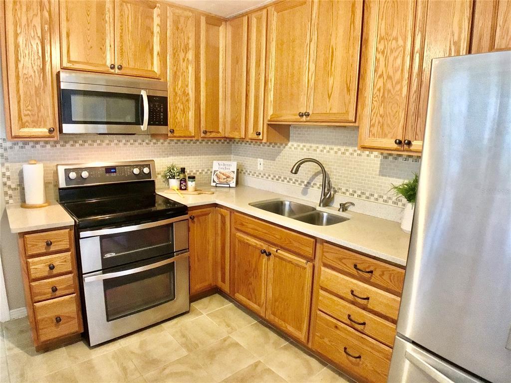 A kitchen features oak cabinets, stainless steel appliances, a double sink, and a tiled backsplash — 3809 W VASCONIA STREET, TAMPA, FL