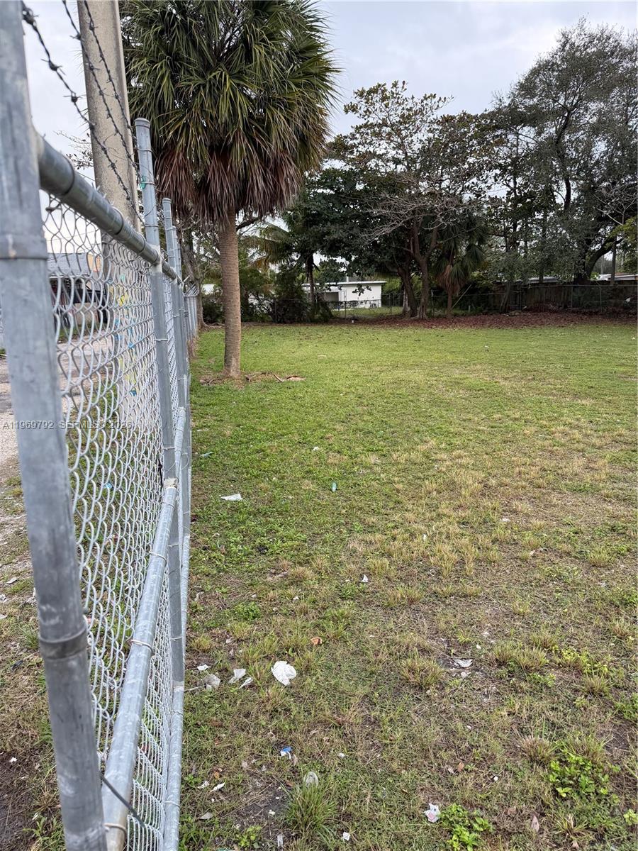 A chain-link fence borders a grassy, vacant lot with trees and a distant building — 752 Opa Locka Blvd, Miami FL 33168, MIAMI, FL