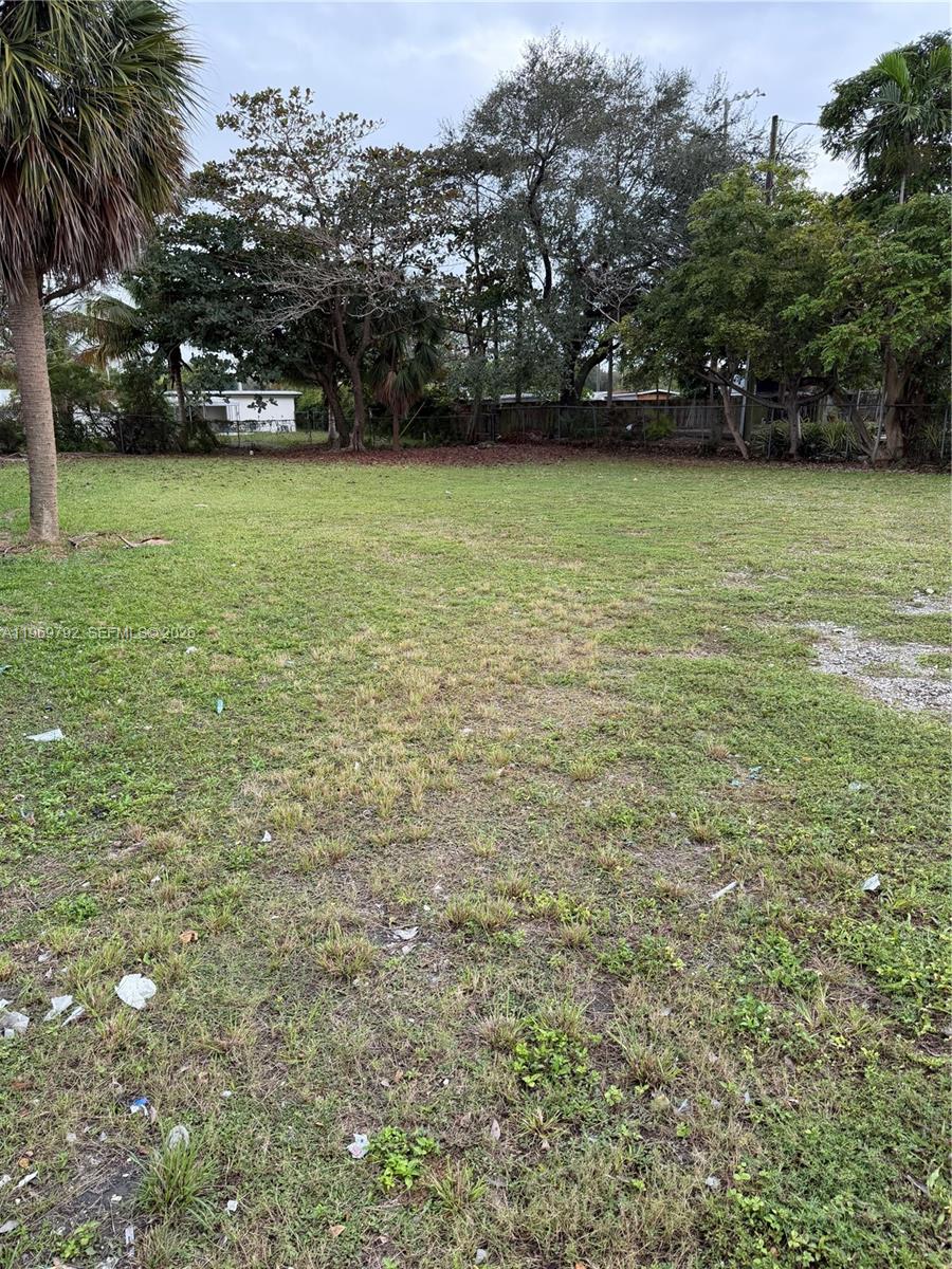 A grassy, vacant lot features scattered debris, surrounding trees, and a distant white building — 752 Opa Locka Blvd, Miami FL 33168, MIAMI, FL
