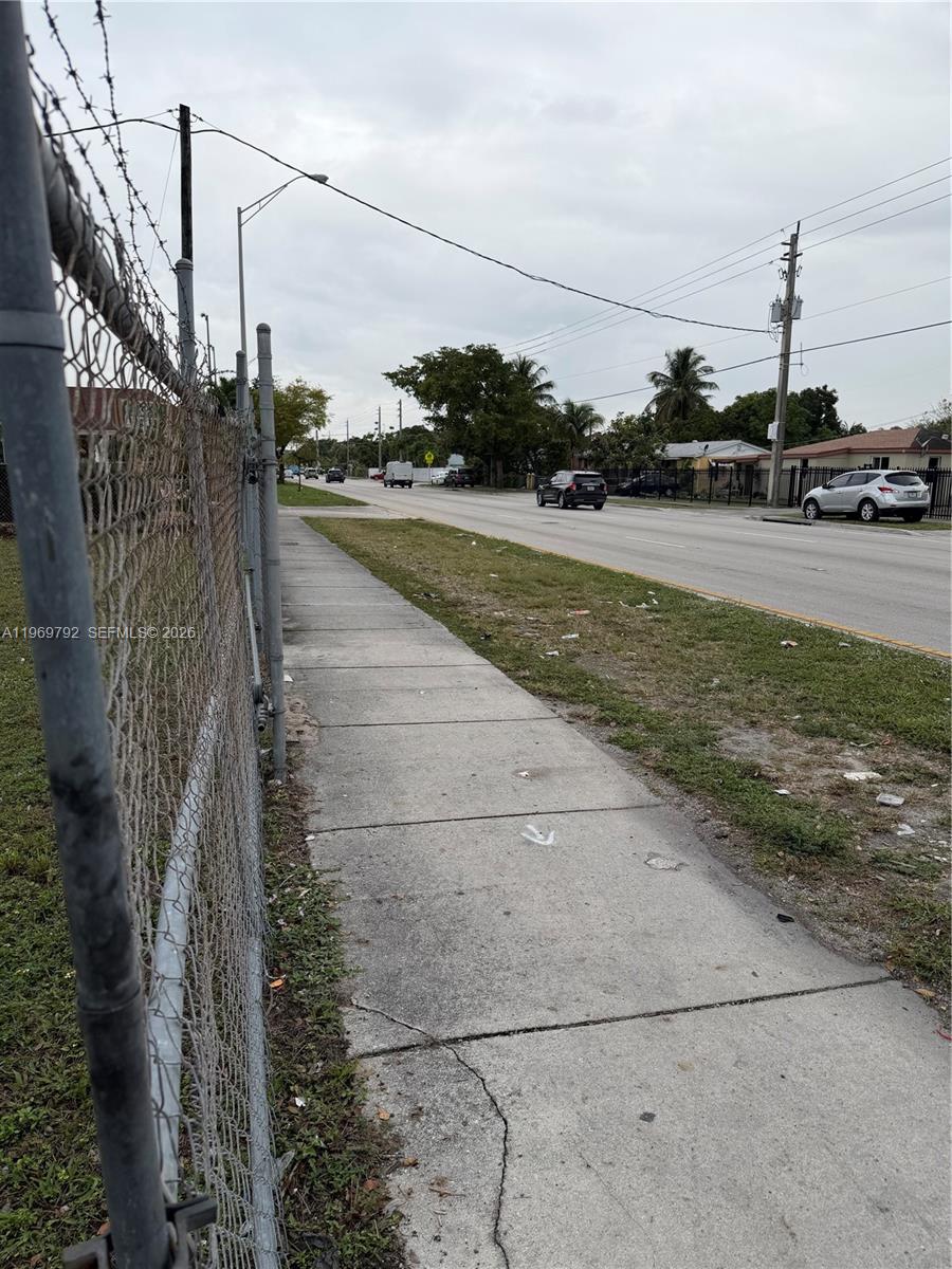 A sidewalk runs alongside a chain-link fence bordering a road with cars and trees — 752 Opa Locka Blvd, Miami FL 33168, MIAMI, FL