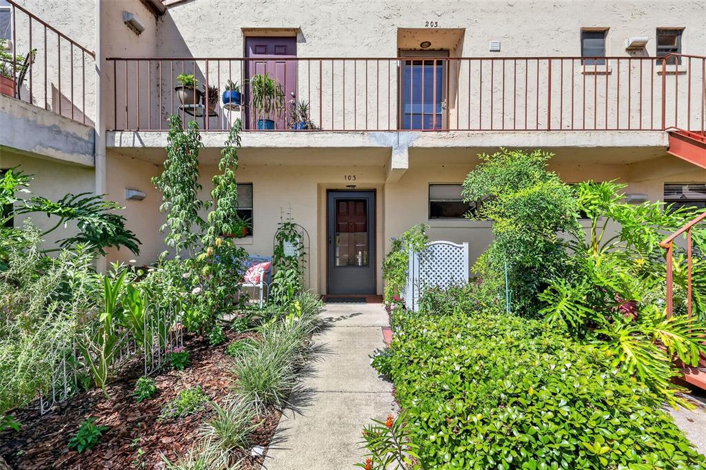 A two-story building exterior features a ground-level entrance, a second-floor balcony, and lush landscaping — 4300 BAYWOOD BOULEVARD UNIT A103, MOUNT DORA, FL