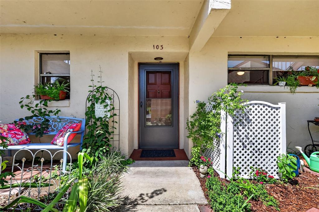 The exterior of a residential unit features a front door numbered 103 and a bench — 4300 BAYWOOD BOULEVARD UNIT A103, MOUNT DORA, FL