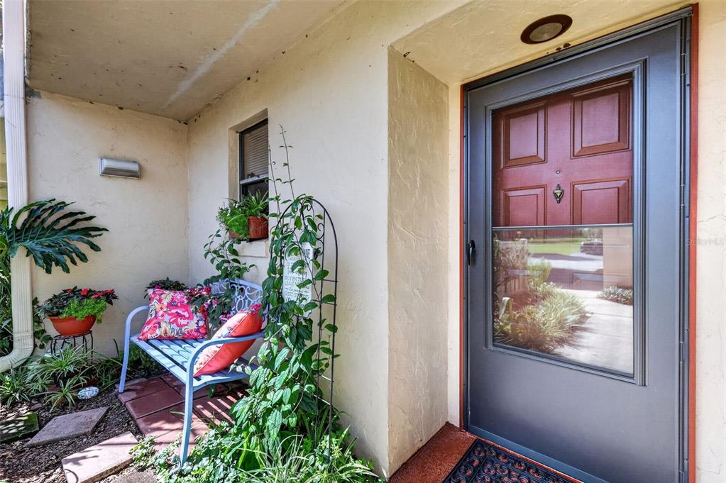 A front entryway features a blue metal bench, potted plants, and a dark storm door — 4300 BAYWOOD BOULEVARD UNIT A103, MOUNT DORA, FL