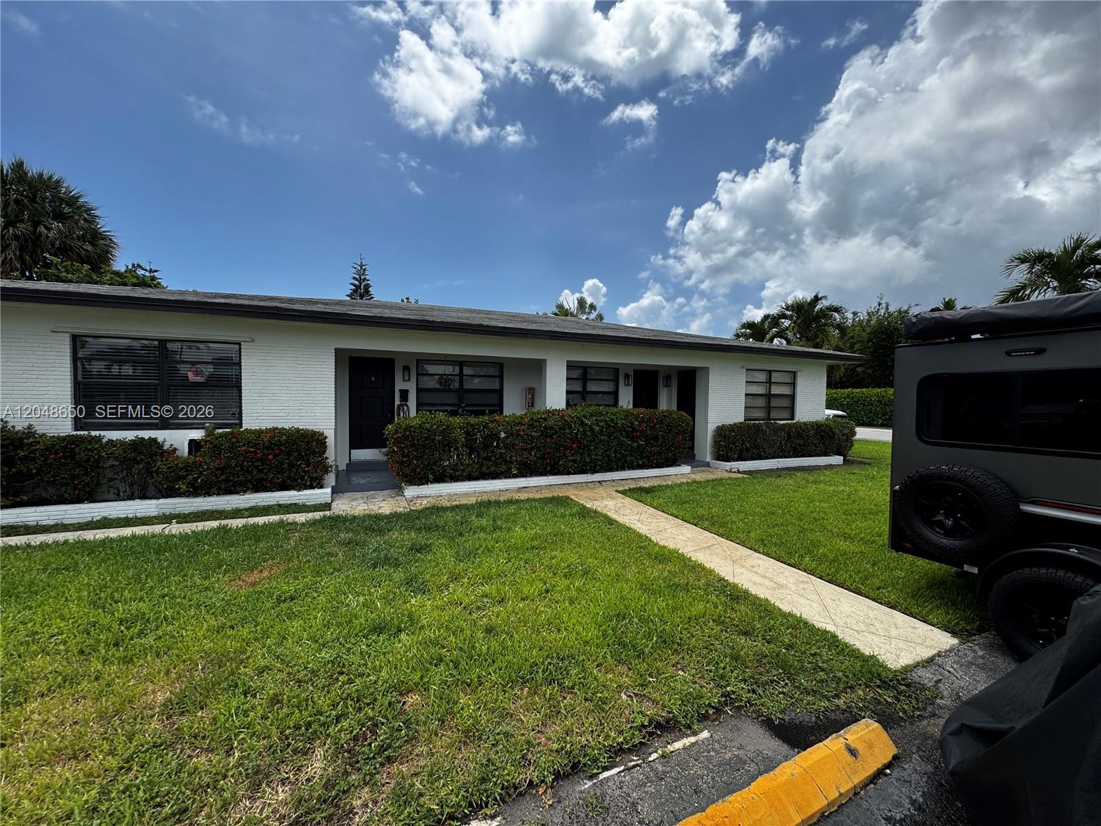 A single-story white brick building features dark-framed windows and a landscaped front yard — 380 SE 12th Ave # 2, Deerfield Beach FL 33441, DEERFIELD BEACH, FL