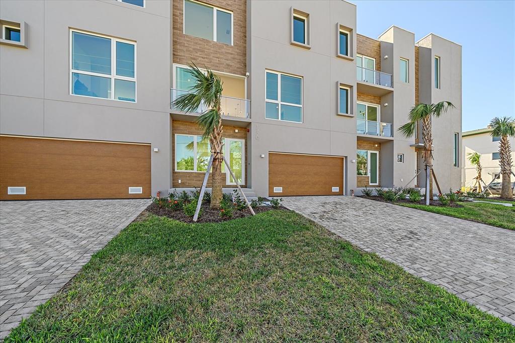 A modern multi-story townhouse exterior features gray stucco, wood-paneled garage doors, and paved driveways — 1720 ALDERMAN STREET, SARASOTA, FL