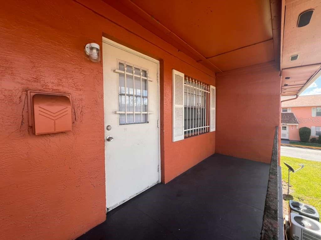 A covered exterior walkway features a white door with a security grate and a mailbox — 1665 W OAK RIDGE ROAD UNIT C, ORLANDO, FL