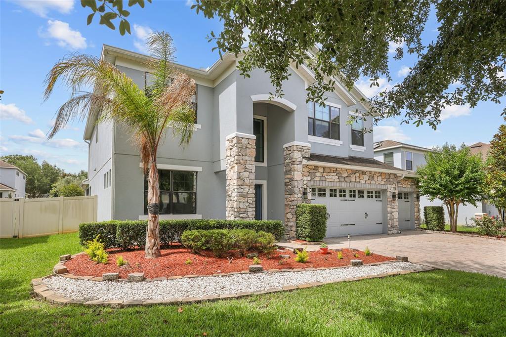 A two-story house with gray stucco, stone accents, a palm tree, and a paved driveway — 5729 RUE GALILEE LANE, SANFORD, FL
