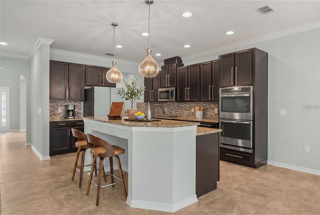 A kitchen with dark wood cabinets, granite countertops, a central island, and stainless steel appliances — 5729 RUE GALILEE LANE, SANFORD, FL
